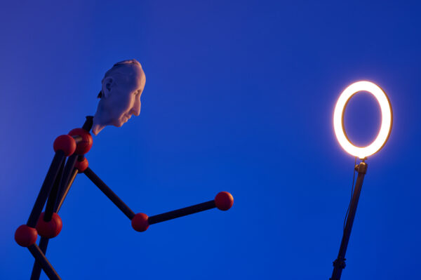 Puppet looking into a ring light with a blue background.